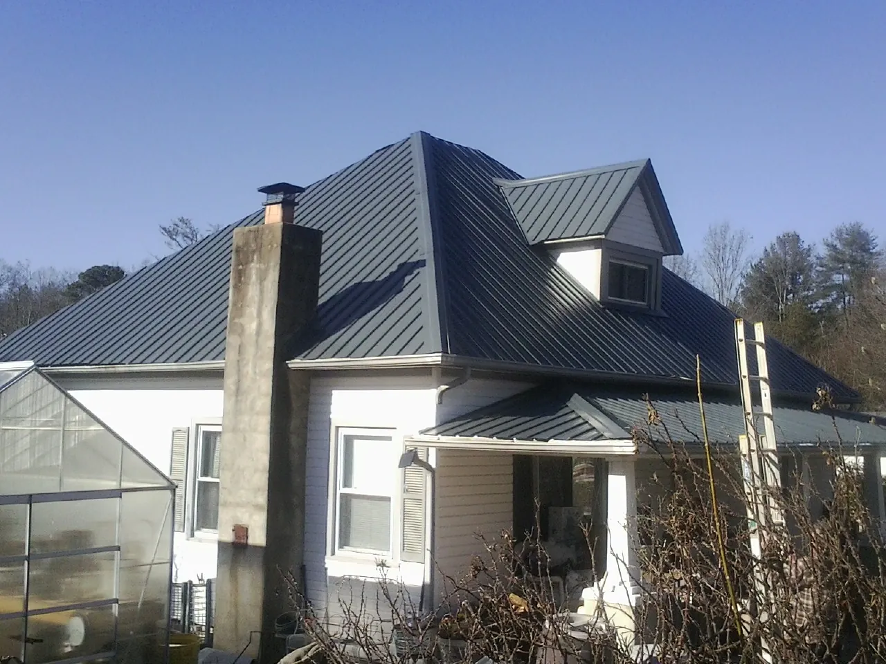 Dark blue standing seam metal roof on a white farmhouse with dormer — Slate & Tile Roof Repair by Roofing Brothers in Frankewing