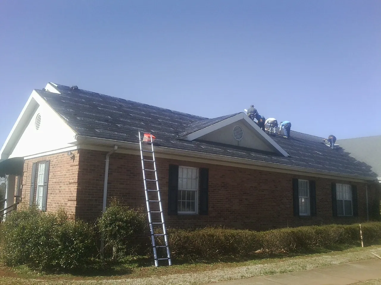 Crew tearing shingles off a brick ranch roof with a ladder set — Metal Roof Repair work by our crew in Frankewing