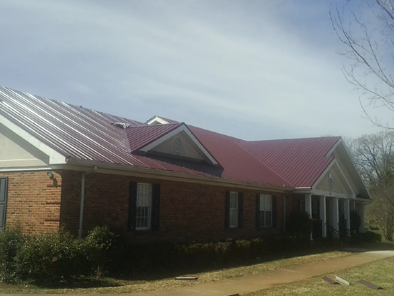 Red metal roof with gabled entries on a long brick building, from a Hail Damage Roof Repair job in Frankewing