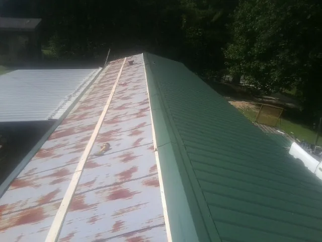 Old rusted panels beside newly installed green metal roofing — Wind Damage Roof Repair by Roofing Brothers in Frankewing