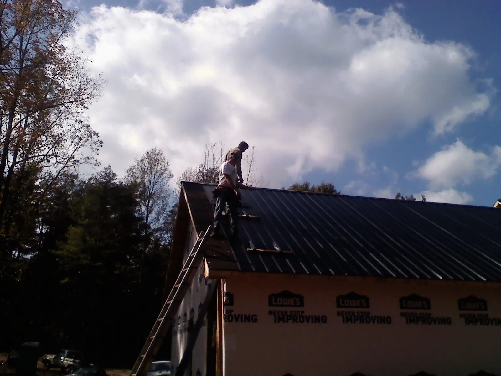 Roofer fastening dark metal panels high against a cloudy sky, from a Roof Inspection job in Frankewing
