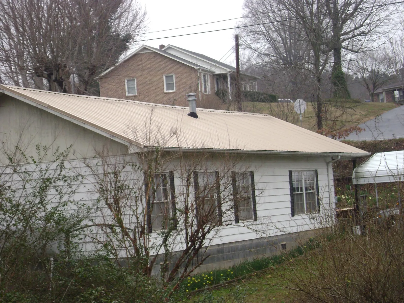 Tan metal roof on a white sided house set into a hillside — Commercial Roofing by Roofing Brothers in Frankewing