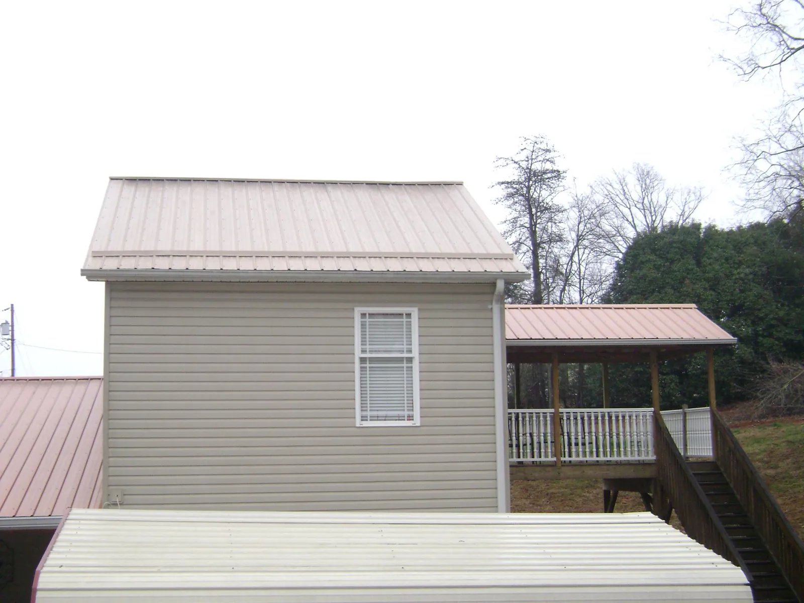 Tan metal roofs on a two story addition and attached porch, from a Roof Replacement job in Frankewing
